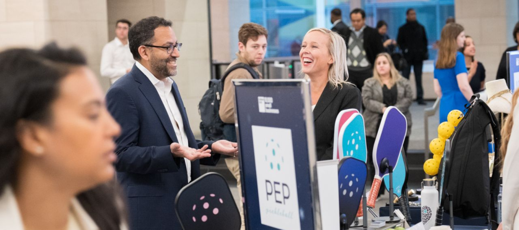 Jill Christiansen, founder of PEP Pickleball, engaging with Ashish Shah at the PEP booth during the Goldman Sachs Holiday Market, showcasing colorful paddles and pickleball accessories.